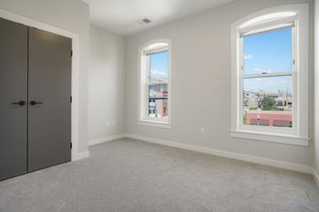 A room with a grey carpet, a grey door and a window with a view of the city at The Avenue Lofts Golden Apartments, Golden, Colorado
